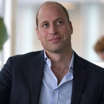 Prince William wears a navy suit and a light blue shirt and smiles awkwardly