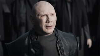 Still from the movie Dune: Part 2. Here we see Glossu Rabban Harkonnen. He is a very pale man with a shaved head and is wearing black robes.