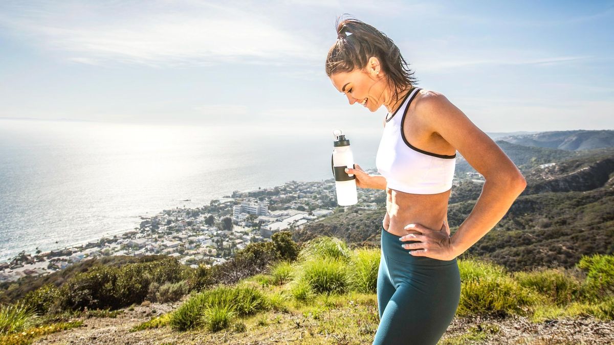 a female runner outdoors in scenery holding a water bottle in one hand 