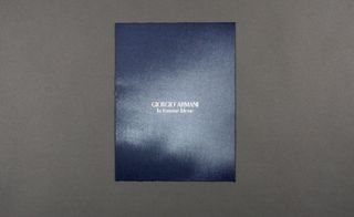 View of Giorgio Armani’s blue invitation pictured against a grey background