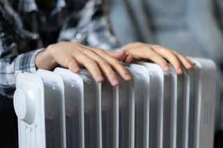 An oil filled radiator with a man warming his hands on top
