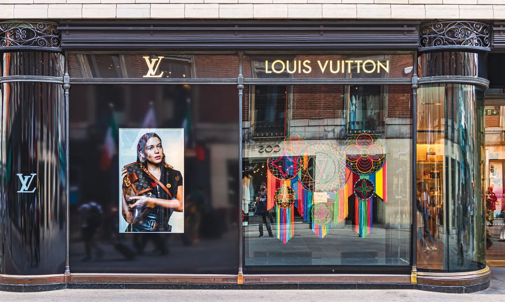 A Louis Vuitton storefront featuring a large portrait of a model and colorful dreamcatcher decorations, reflecting luxury and style.