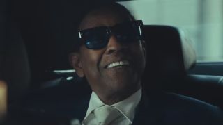 A sunglassed Denzel Washington sits smiling in the back of a limo in Highest 2 Lowest.
