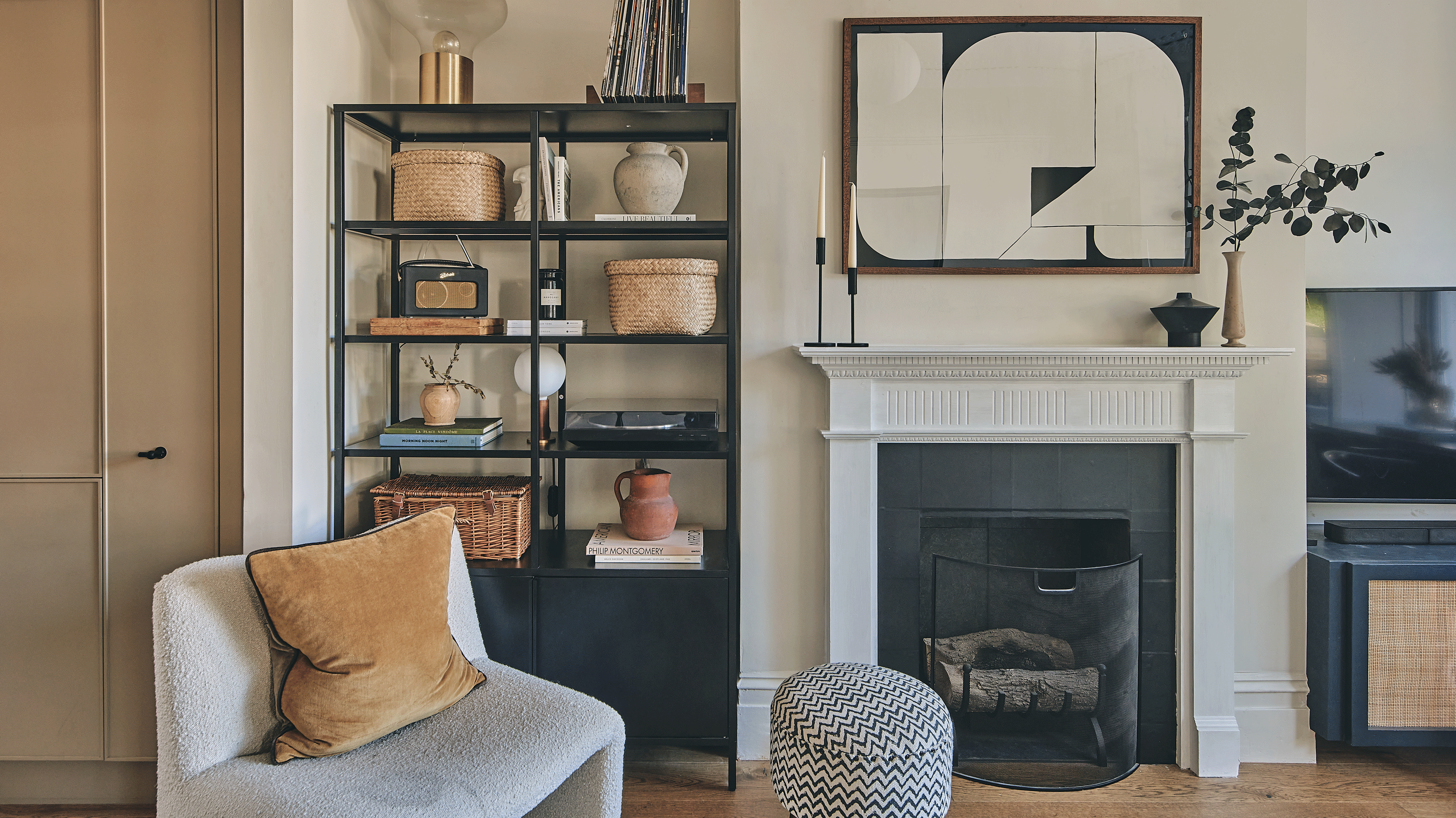 a living room with black metal alcove shelving a fireplace and traditional fire surround a boucle occasional chair and a zig zag patterned black and white footstool