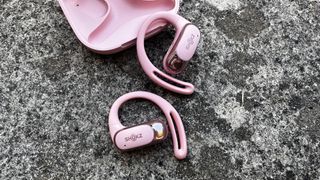 Shokz OpenFit Air earbuds in pink pictured on a concrete surface next to their charging case