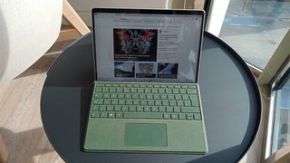 A Microsoft Surface Pro 9 sits on a table in the sun agains a window