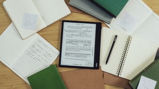 The Kobo Elipsa 2E on a desk next to the Stylus 2 surrounded by books both opened and closed.