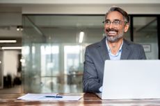 Portrait of mature business man or entrepreneur using laptop computer, typing, working in modern office. Middle-age Hispanic smiling handsome businessman entrepreneur.