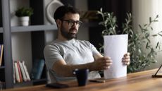 A man tidies up a pile of paperwork at his desk.