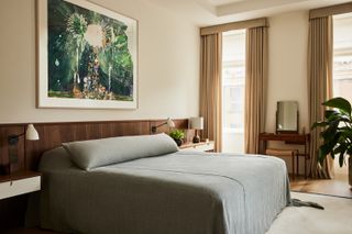 A large bed covered with a grey comforter rests below an abstract artwork