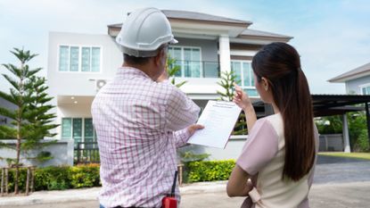 Home inspector wearing a construction hat and holding a clipboard discusses home issues with female homeowner