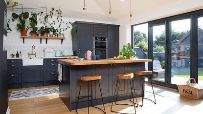 Dark blue Shaker kitchen with wood and black metal bar stools, black bifold doors and bare bulb lights over island