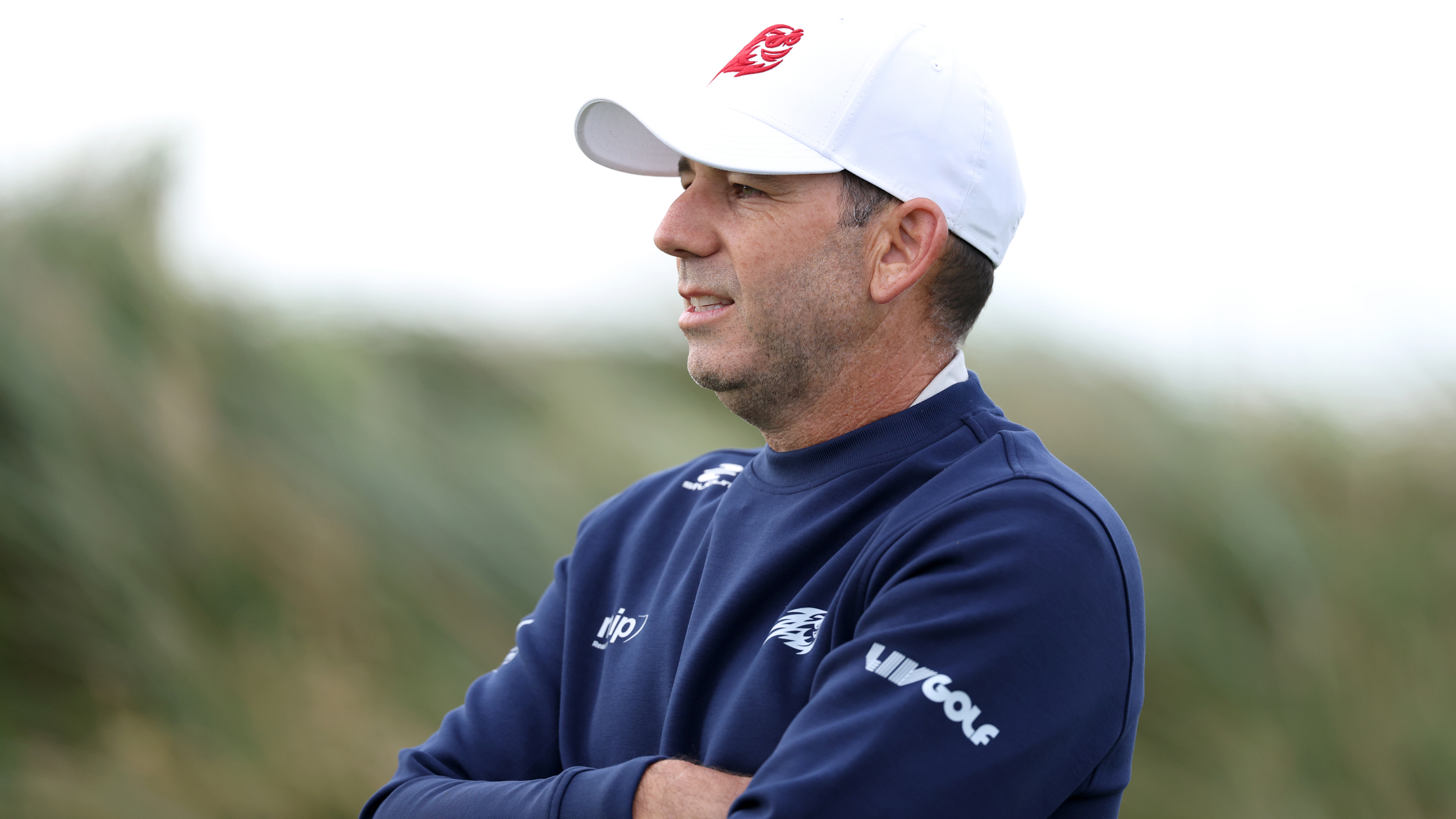 Sergio Garcia wearing a navy blue sweater and white cap with his arms crossed