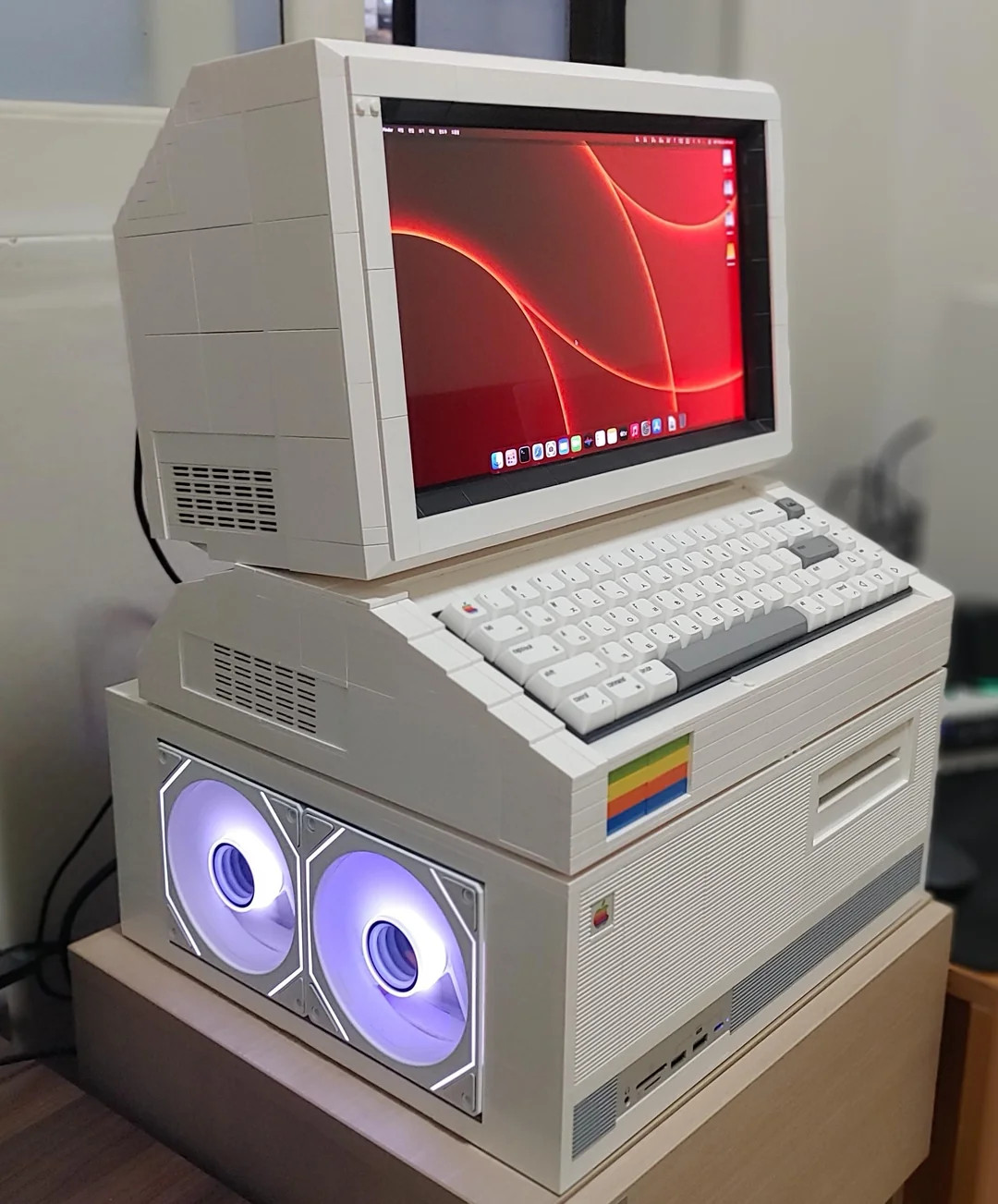 Retro-style computer made from LEGO bricks, featuring a modern monitor with a red swirl design on the screen. Includes front fan lights and rainbow detail.