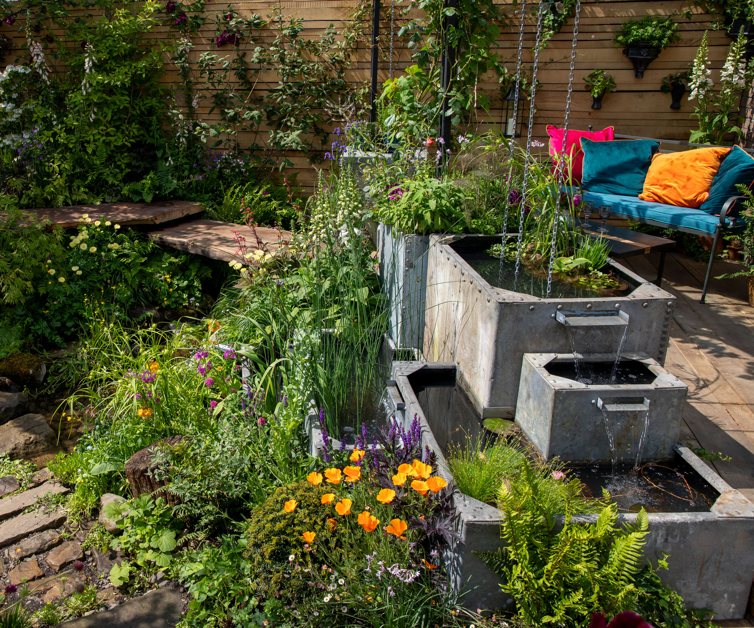 tank water feature with rain chains and water blades, in small garden with decking and garden furniture plus lots of planting