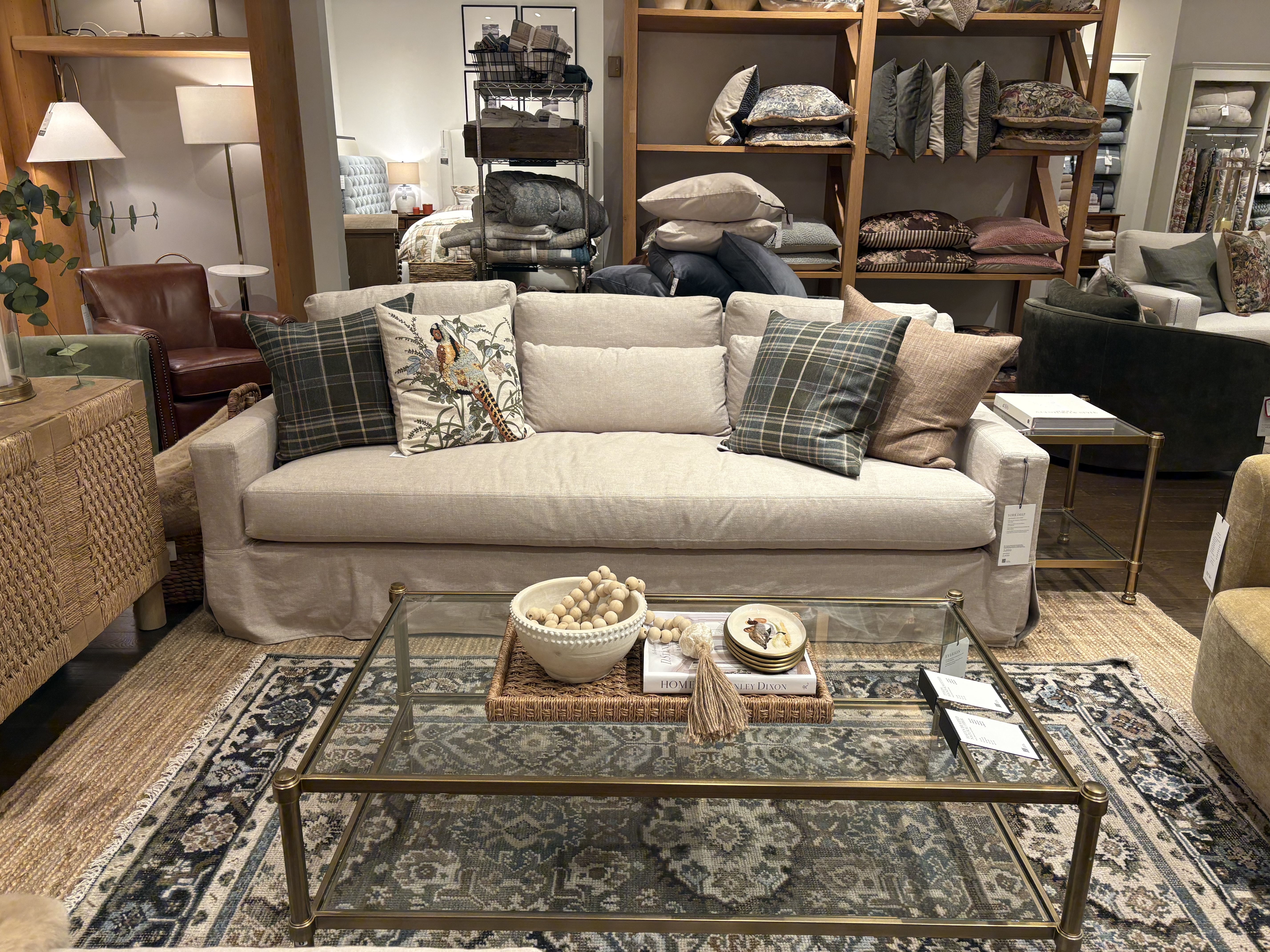 white pottery barn sofa in a showroom surrounded by patterned rug, glass and gold coffee table, cane entertainment unit, and patterned cushions