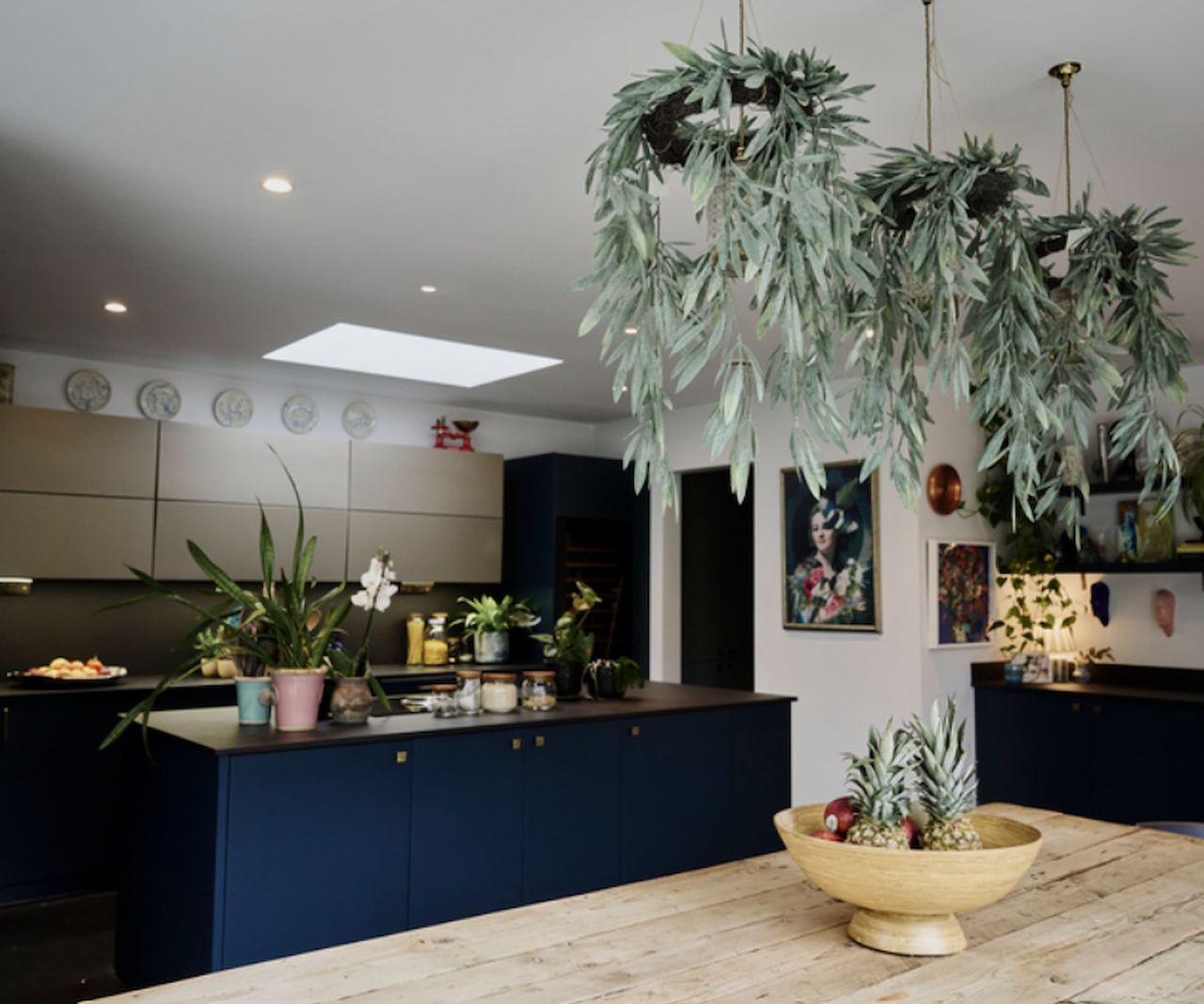 A kitchen with blue cabinets and a rooflight with a dining table with olive branches hanging above it