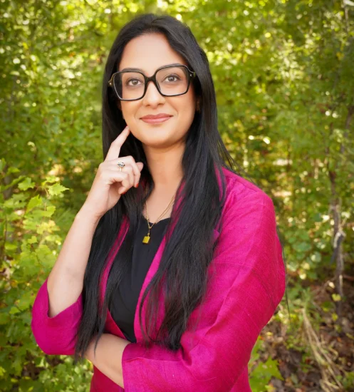 Headshot of Dr. Uma Darji, wearing pink shirt and stood in front of greenery.