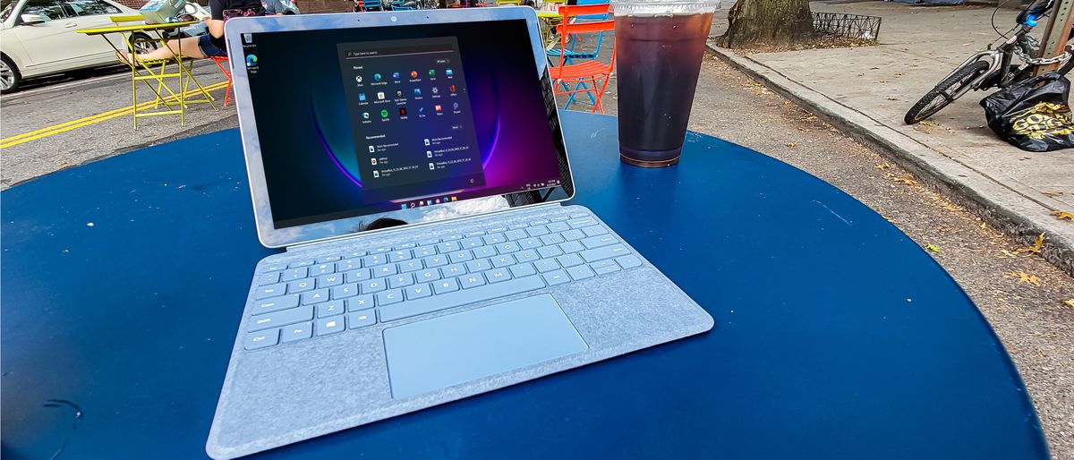 Surface Go 3 on a blue table outdoors next to a cup of iced coffee