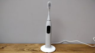 Image shows the Oclean X Pro toothbrush standing upright on its charging stand.