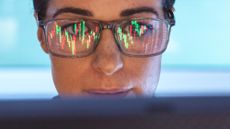 Close-up of a woman's face with a computer reflection of stock charts in her eyeglasses