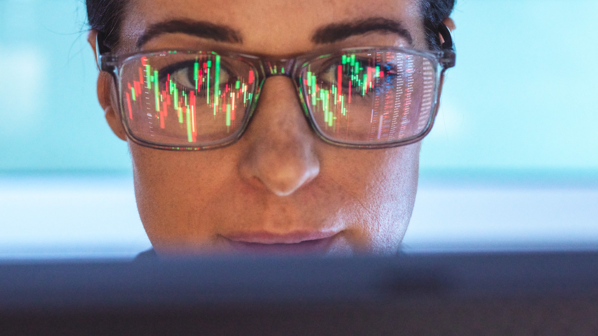 Close-up of a woman's face with a computer reflection of stock charts in her eyeglasses