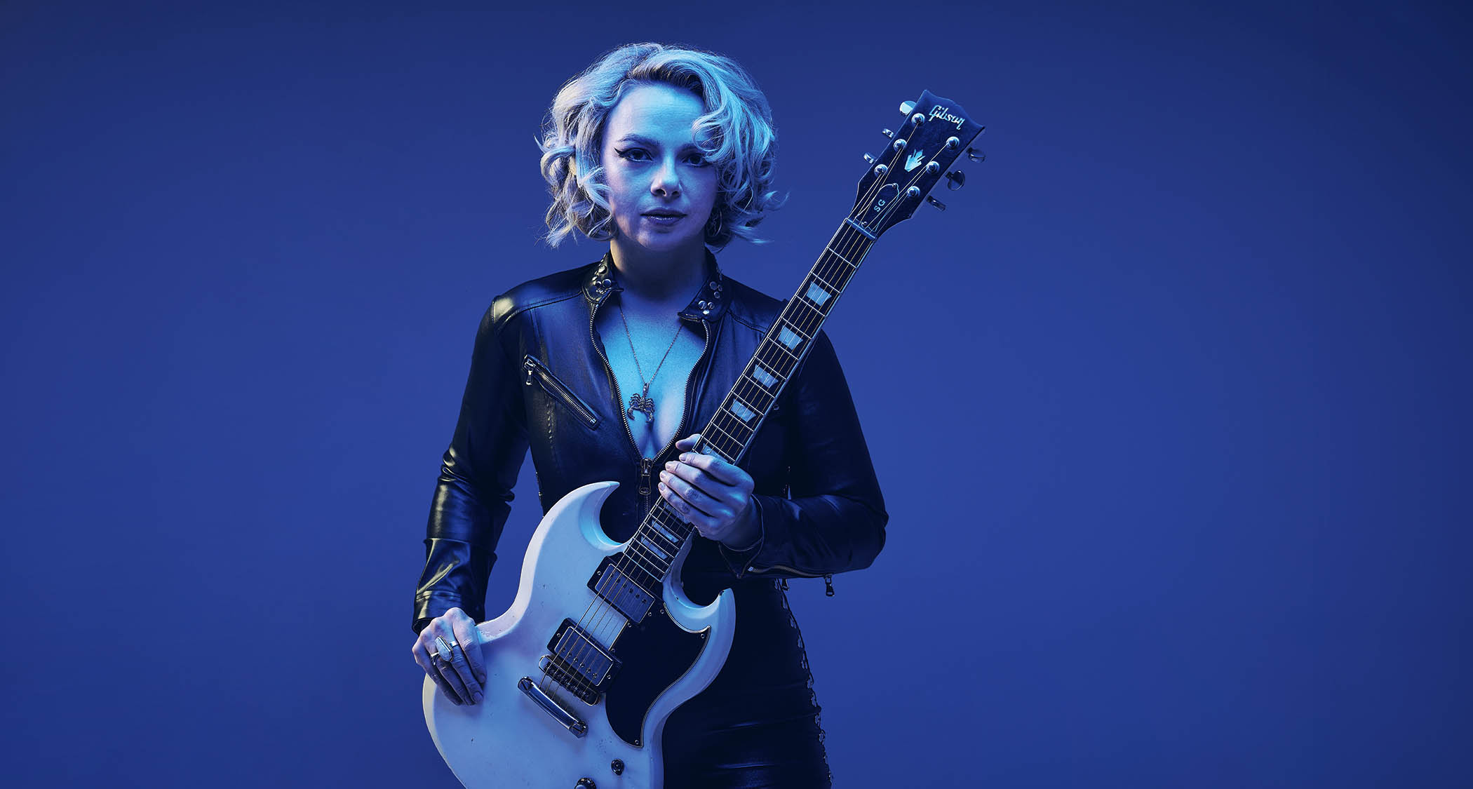 Samantha Fish, lit up in blue, photographed with her Gibson SG.
