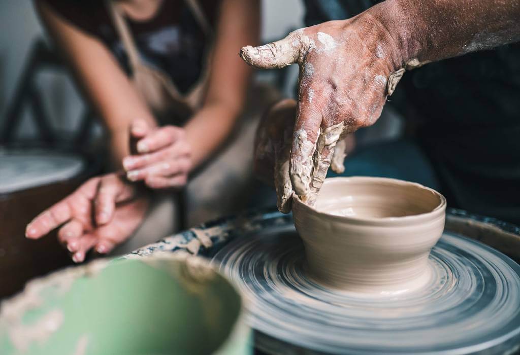 Two people making pottery on a pottery turn table.