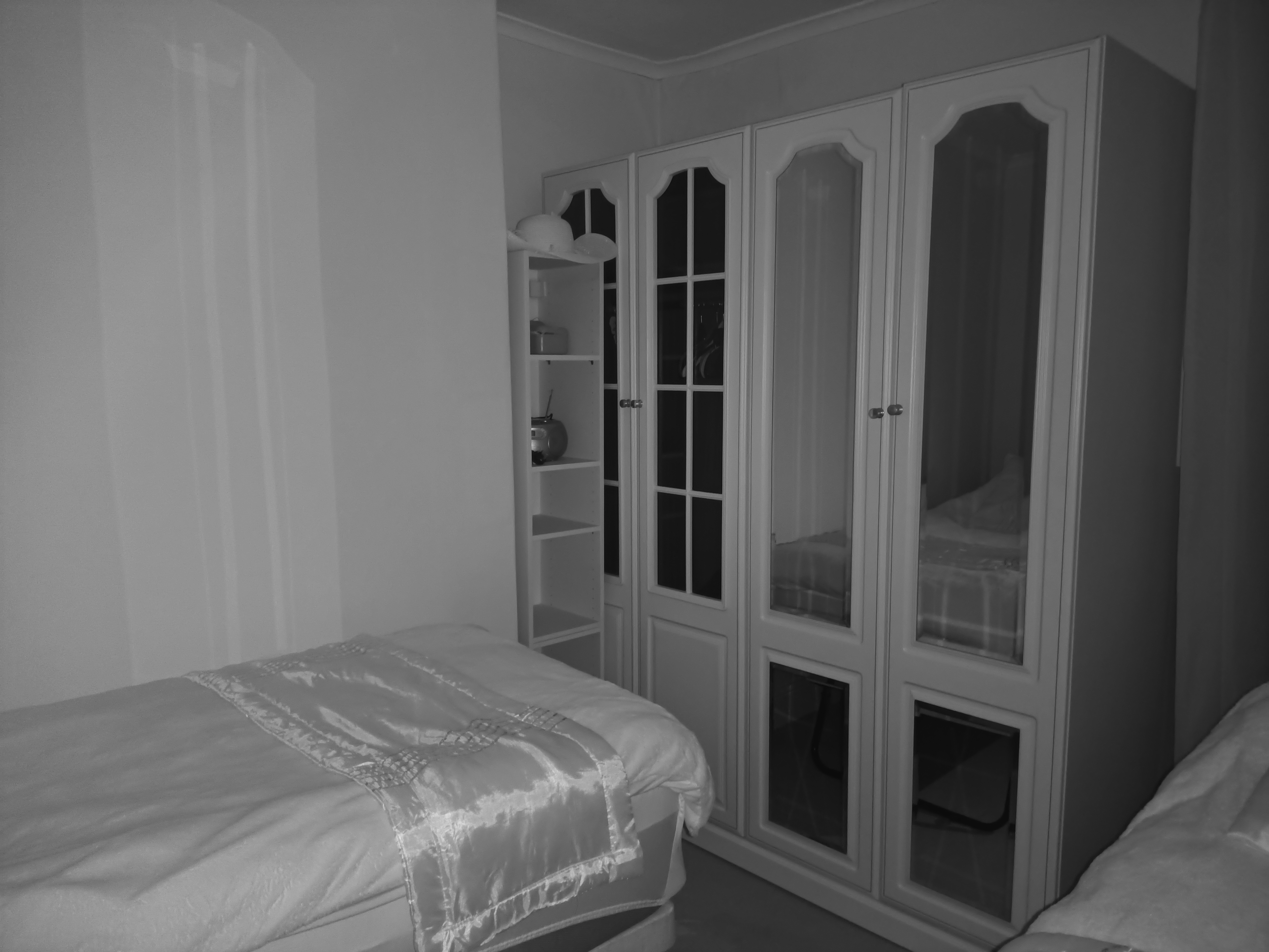 A black-and-white photo of a bedroom with a bed and a large white wardrobe featuring mirrored doors is shown.