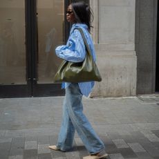 Liv wears blue and white striped button down, jeans, off-white mules, and a large olive green shoulder bag