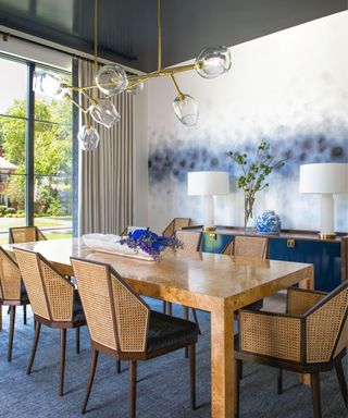 A blue and white dining room with a wooden table, textured wooden dining chairs, and a sculptural gold light fixture hanging above