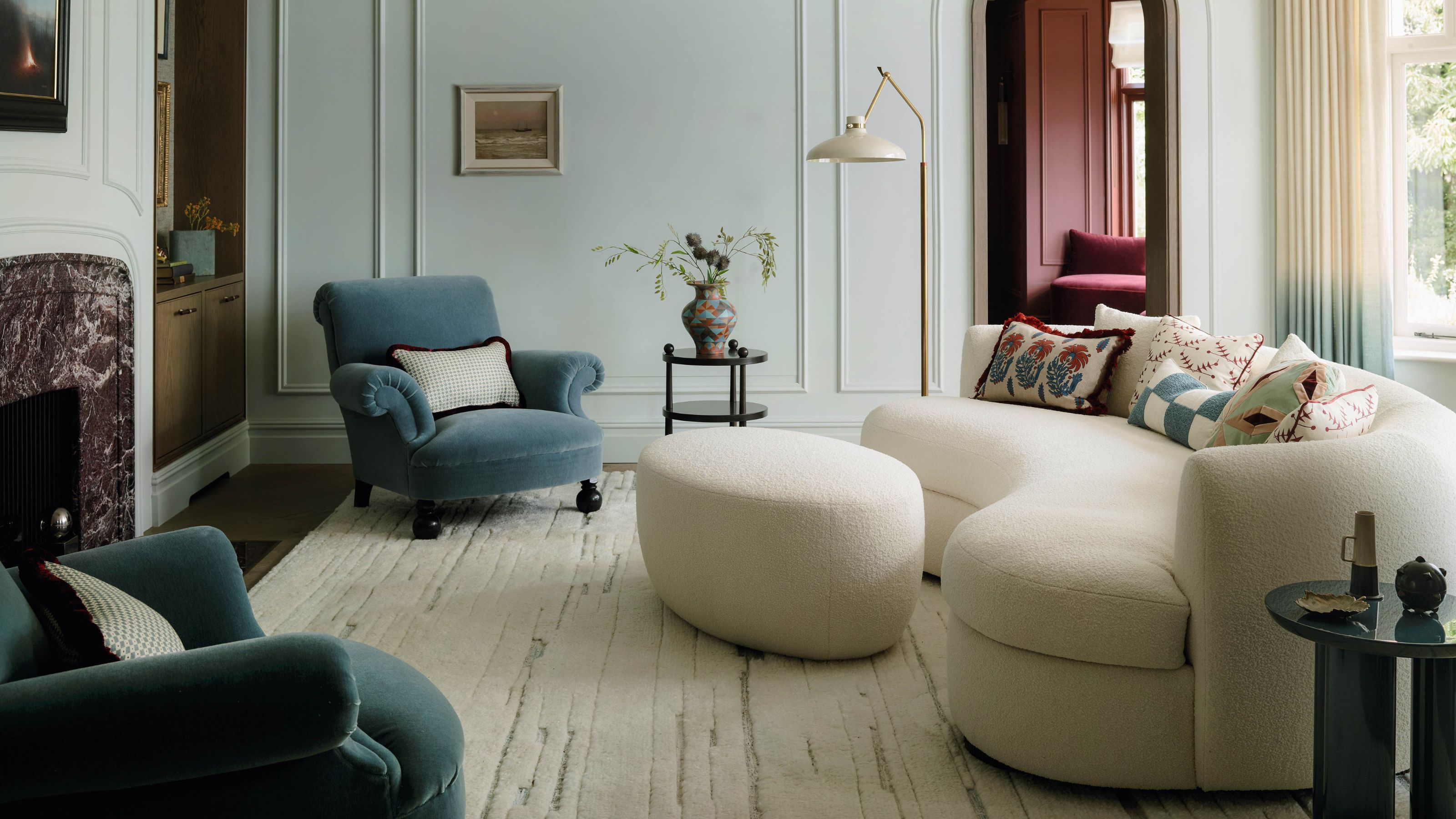 a light blue living room with decorative molding, a dark red marble fireplace, white curved couch and two smokey blue velvet armchairs