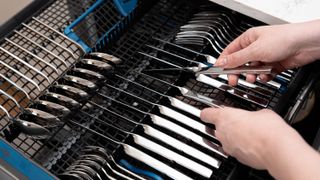 Cutlery being loaded into the third rack of a dishwasher