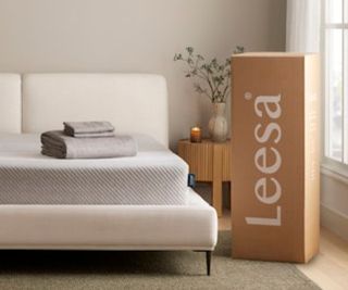 The Leesa Original Memory Foam Mattress against a white wall beside a Leesa delivery box.