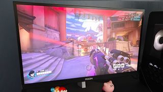 AOC AGON Pro AG246FK with Overwatch 2 gameplay on screen and Pharah under gunfire