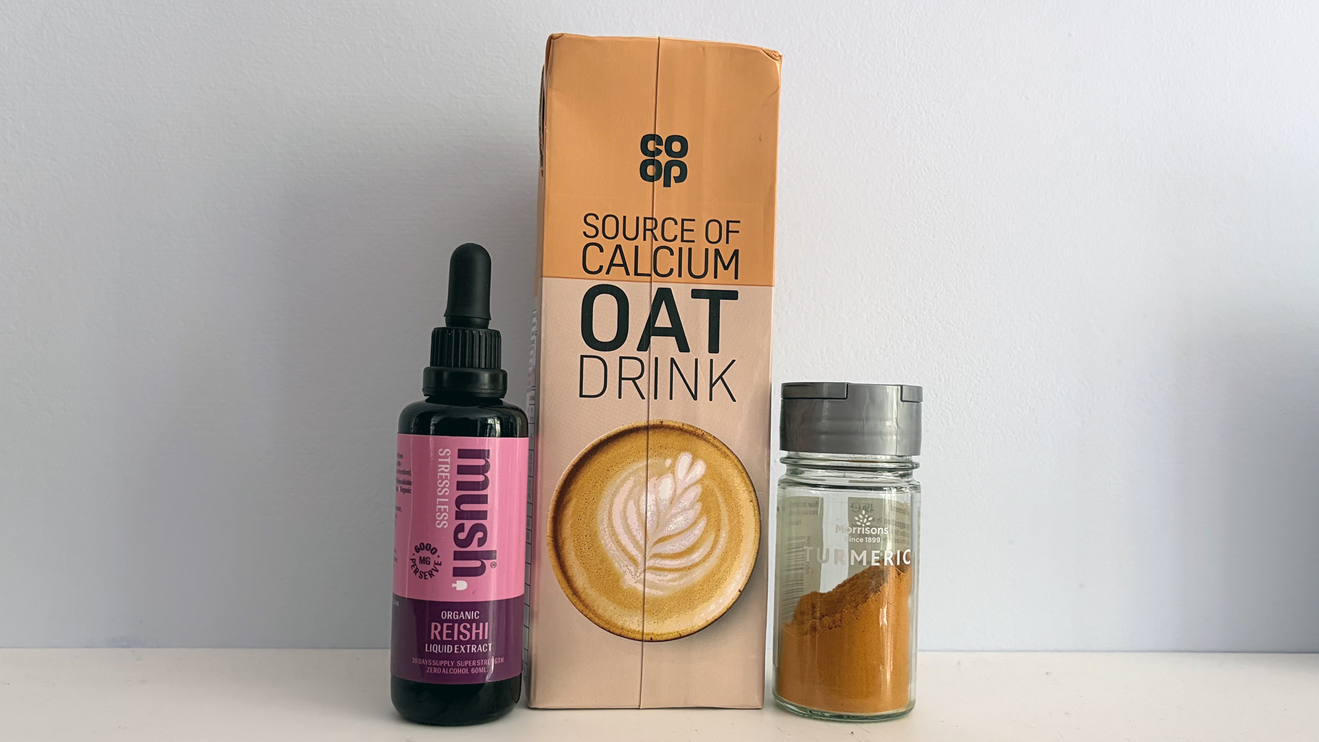 A bottle of Reishi mushroom supplement, a carton of Oat Milk, and a jar of ground turmeric