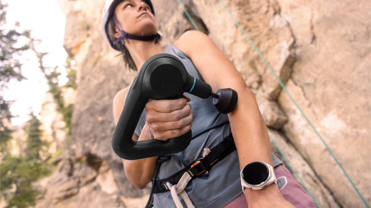 Rock climber using a theragun and wearing a Garmin watch