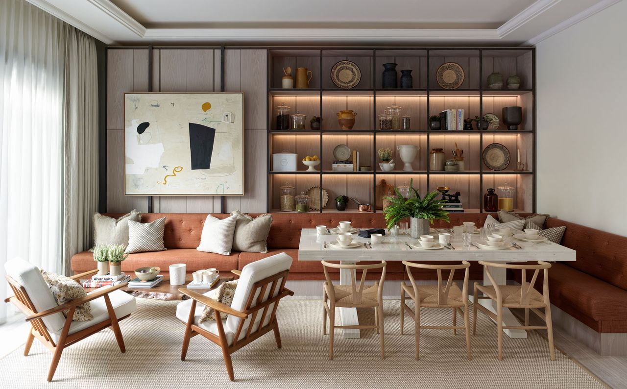 Dining room with L shaped, burnt orange sofa stretching as dining area seating around to casual coffee table seating