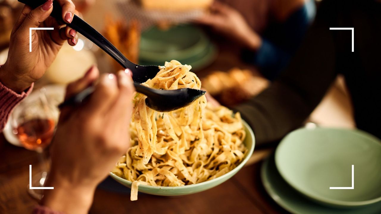 Woman serving from a large bowl of fettuccine pasta onto plates, an example of what to eat when reverse dieting