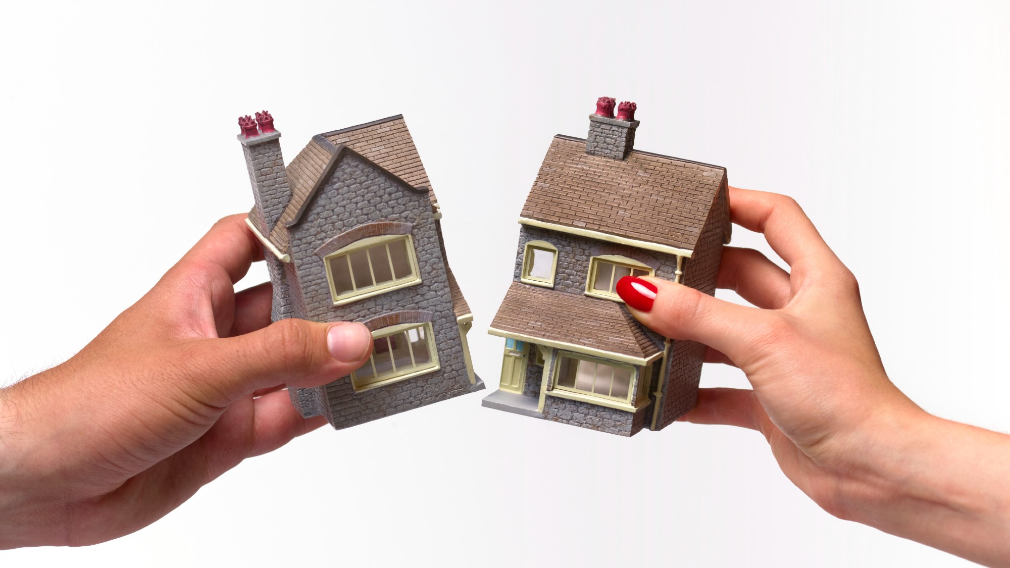 Two hands, one belonging to a man and one to a woman, pulling at and breaking a toy house in half
