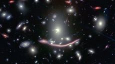 A photo of deep space with an elongated arc of warped light from a galaxy in the center