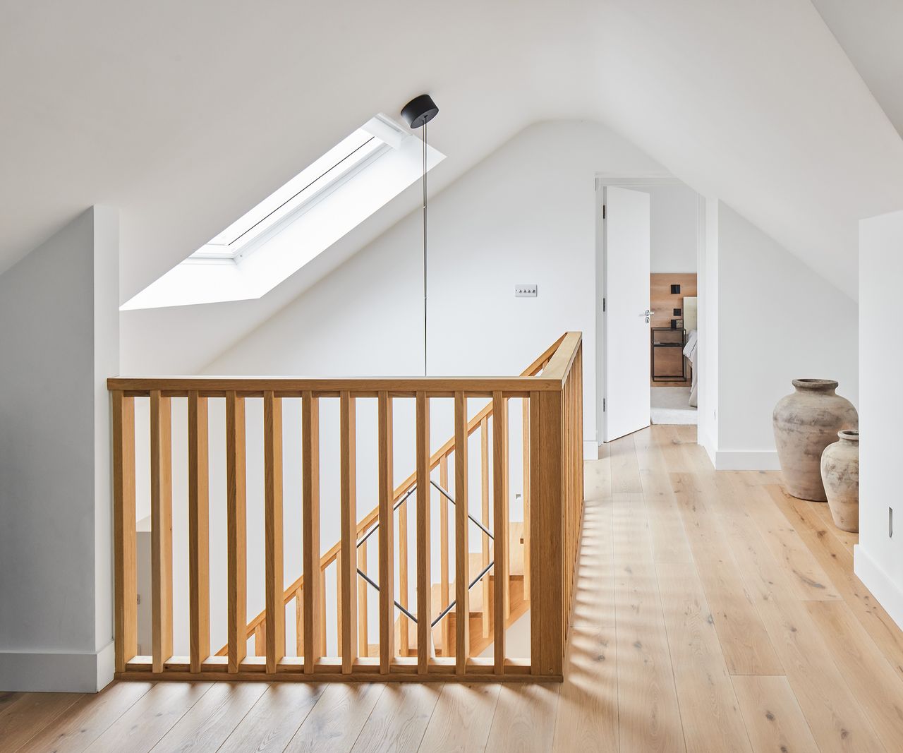 A landing in a loft with a pitched roof and skylight. The floors and banisters are wooden and the walls are white