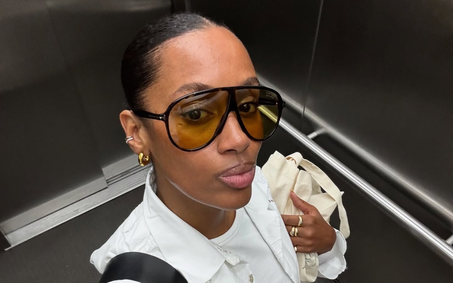 Woman takes an elevator selfie in large aviator sunglasses with yellow-tinted lenses.