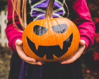 Easy no-carve pumpkin ideas with a Jack O'Lantern faced created with black stickers on an orange pumpkin