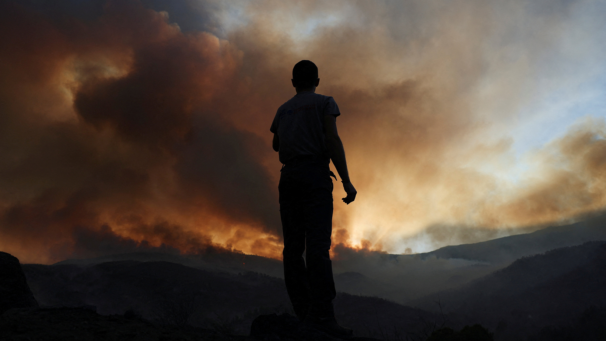 A man observes a wildfire on the outskirts of Mombeltran, Spain