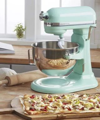 A turquoise KitchenAid stand mixer and steel mixing bowl; a flatbread topped with vegetables on a wooden worktop.