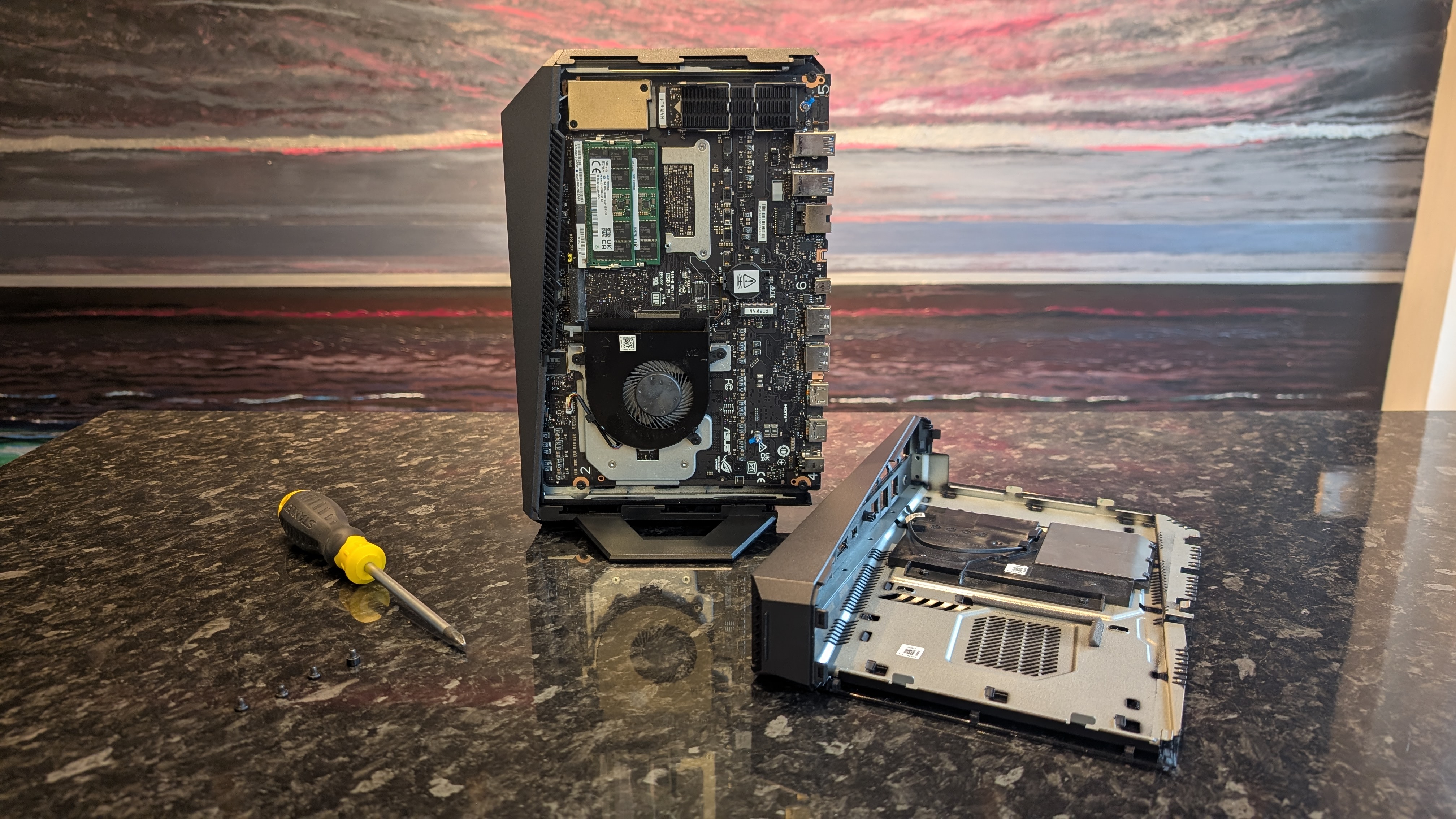 The Asus ROG NUC photographed on a dark marbled worksurface with a painted sunset in the background.