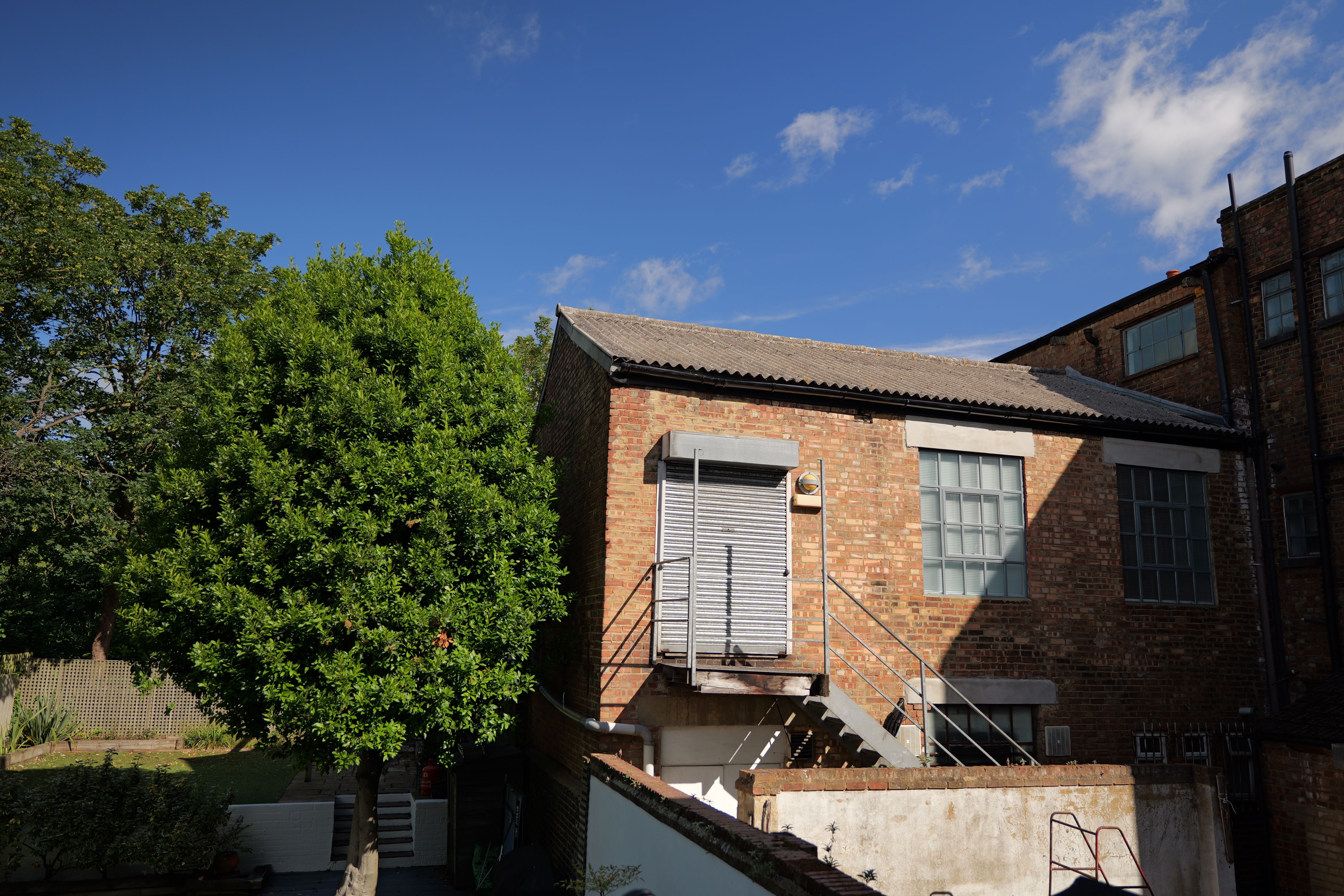 A warehouse next to a tree in front of a bright blue sky