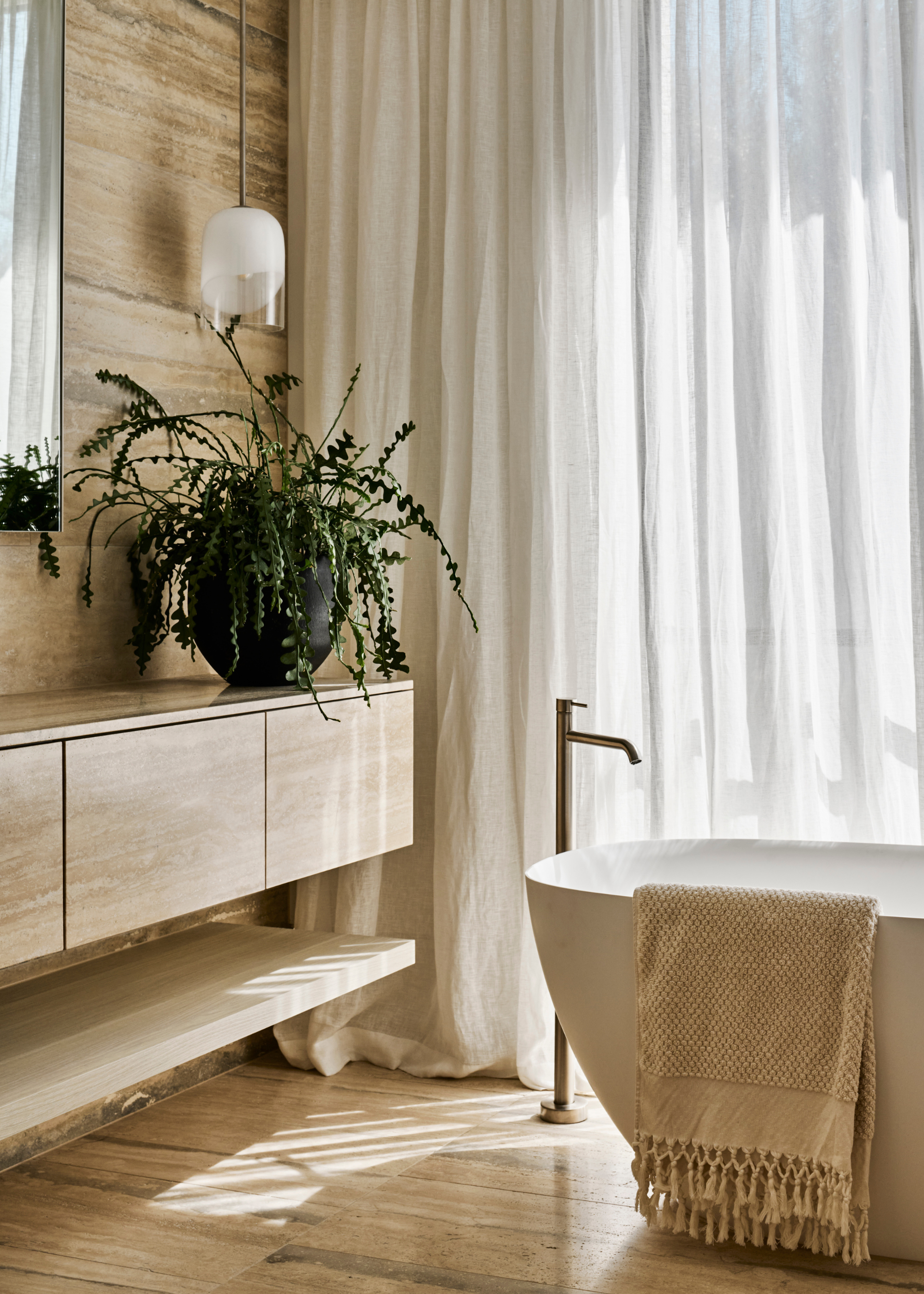 A bathroom with a potted trailing houseplant on a floating stone counter beside a bathtub