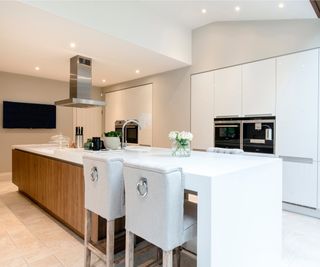 preloved white kitchen with long central island with seating area and wooden storage below sink and extraction fan above